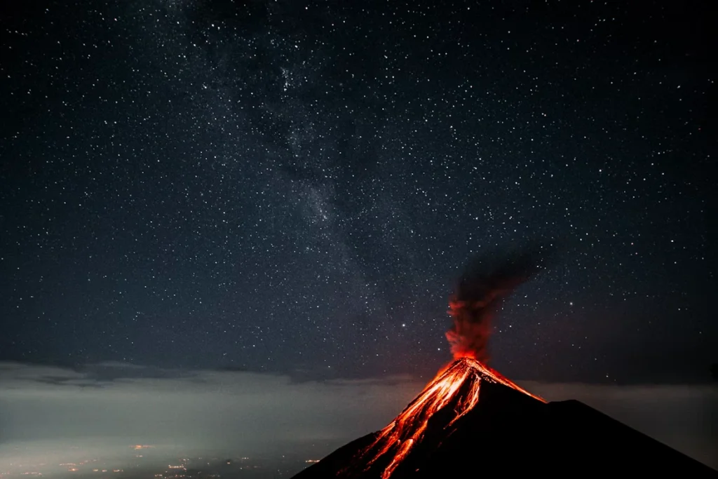 Vulcão em erupção durante a noite com lava incandescente, representando a força dos vulcões sob um céu estrelado